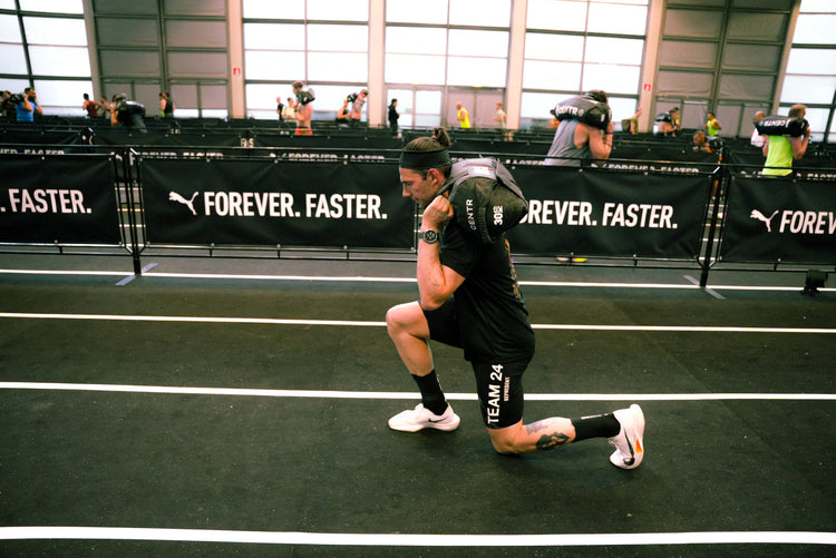 Atleta durante la stazione sandbag lunges in una gara Hyrox, affondi con il sacco sulle spalle